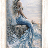 Print of a mermaid sitting on a rock by the sea in soft blues and white, shown in a light wood-tone frame.