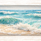 Print of turquoise waves crashing onto a golden sandy beach under a blue sky, shown in a light wood-tone frame.