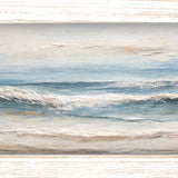 Print of gentle waves rolling onto a sandy beach in soft blues and beige, shown in a light wood-tone frame.